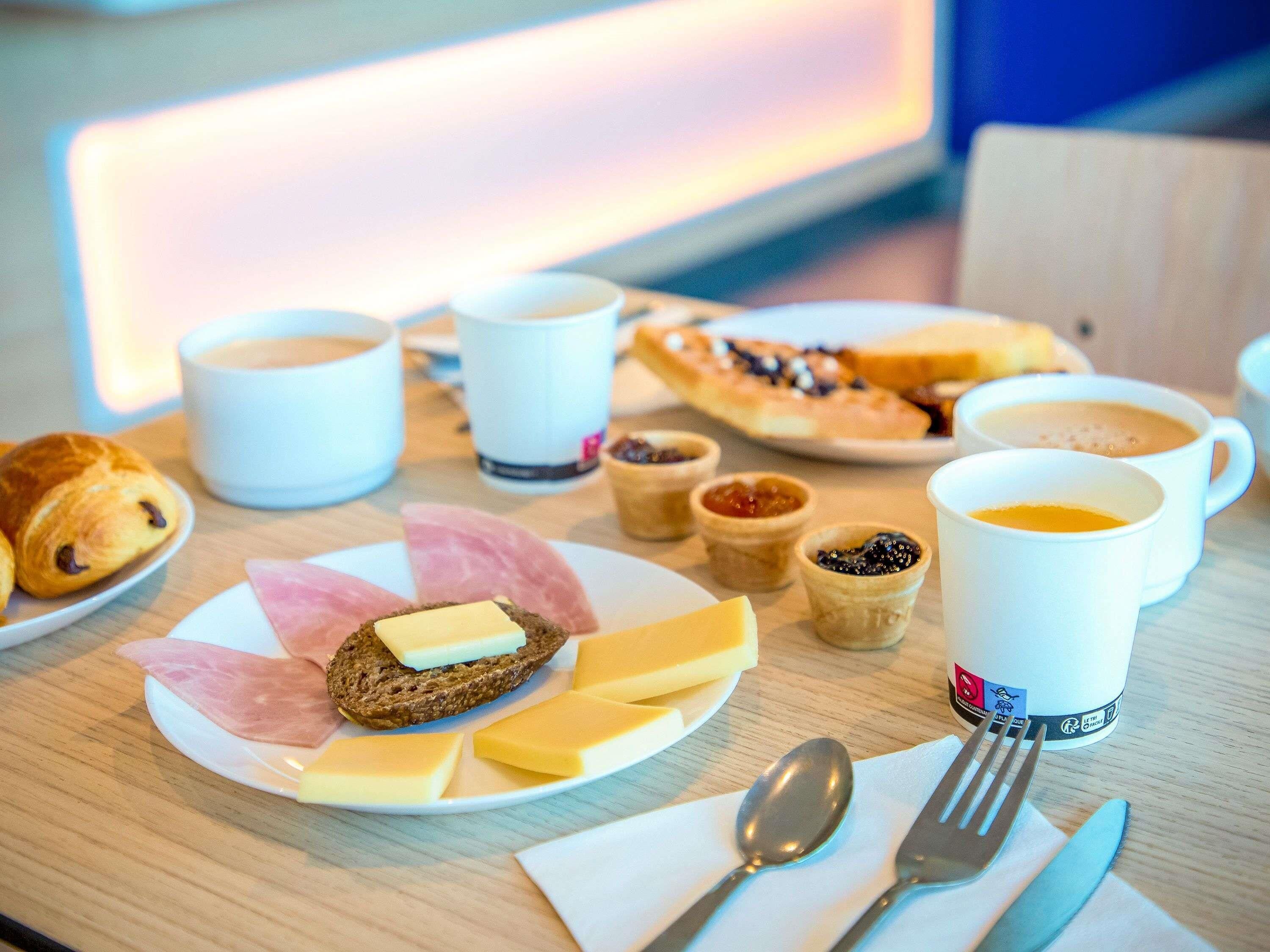 A breakfast setting with croissants, cheese, ham, bread, coffee, and condiments on a table.