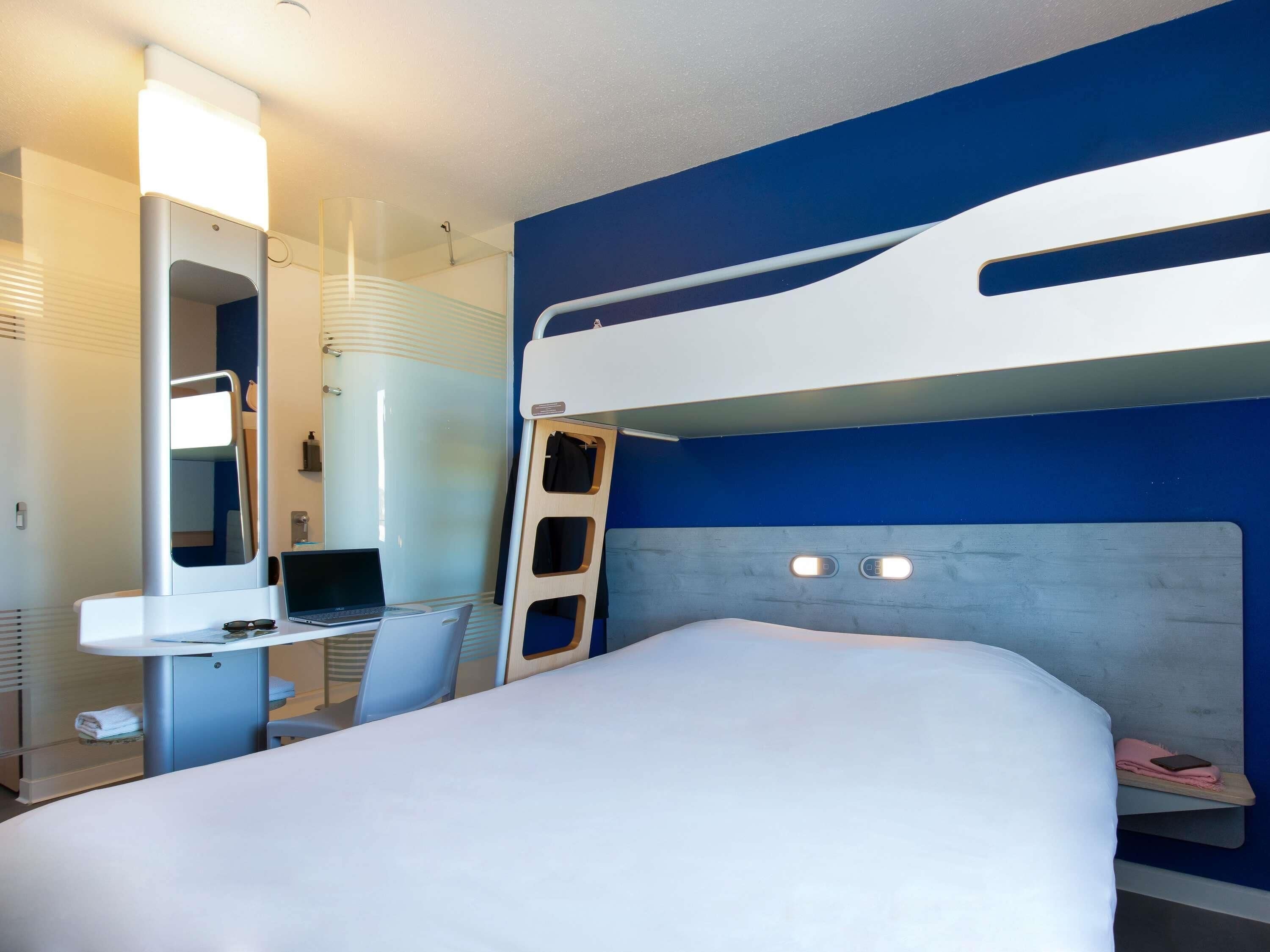 Une chambre d’hôtel avec un lit superposé, un bureau avec un ordinateur portable, un miroir et un espace douche.