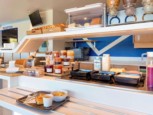 Ein Frühstücksbuffet mit verschiedenen Speisen, ein Empfangsbereich und ein Fernsehbildschirm.