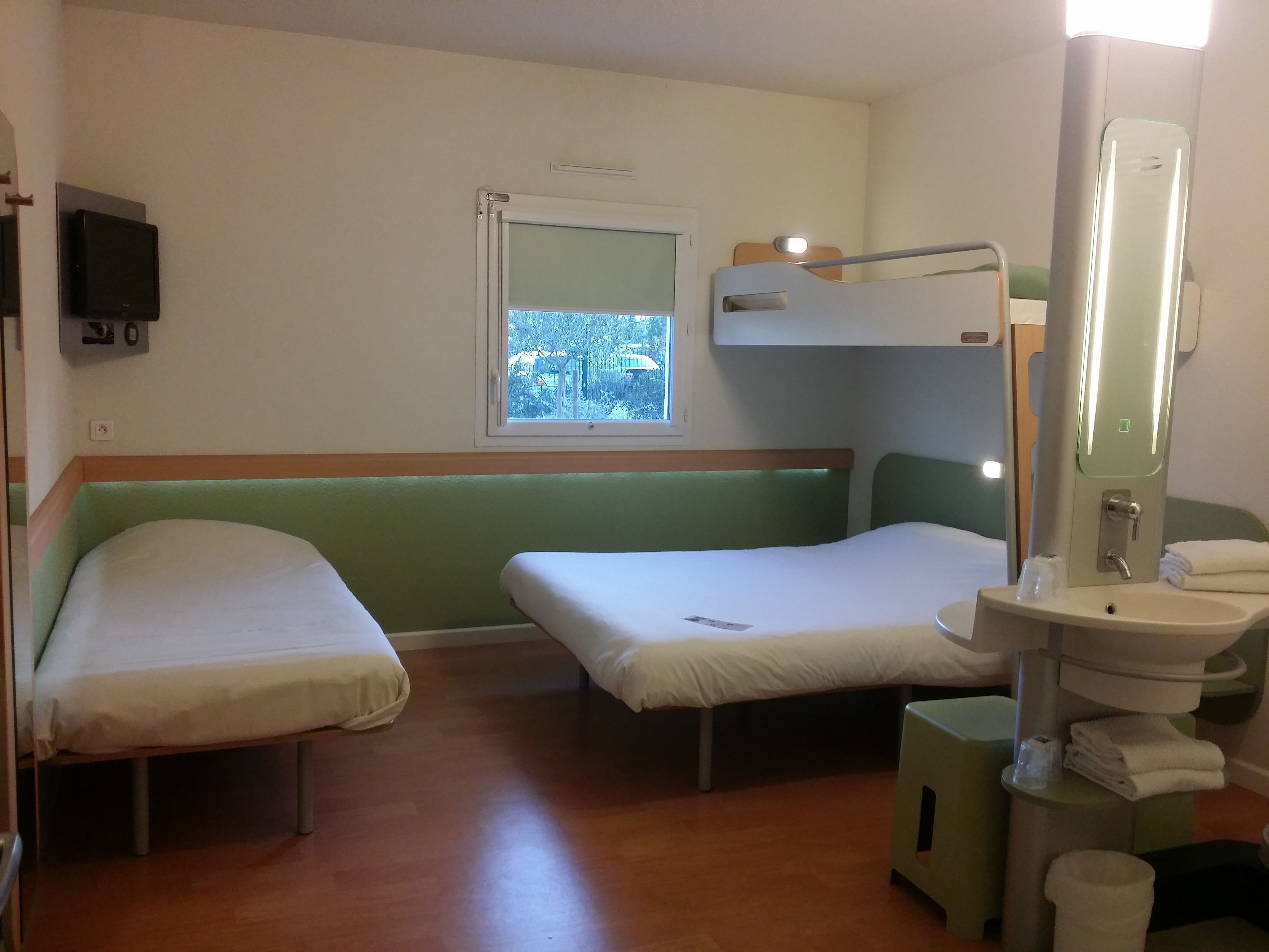 Una habitación de hotel pequeña y con una cama individual, una ventana, un espejo y un lavamanos.