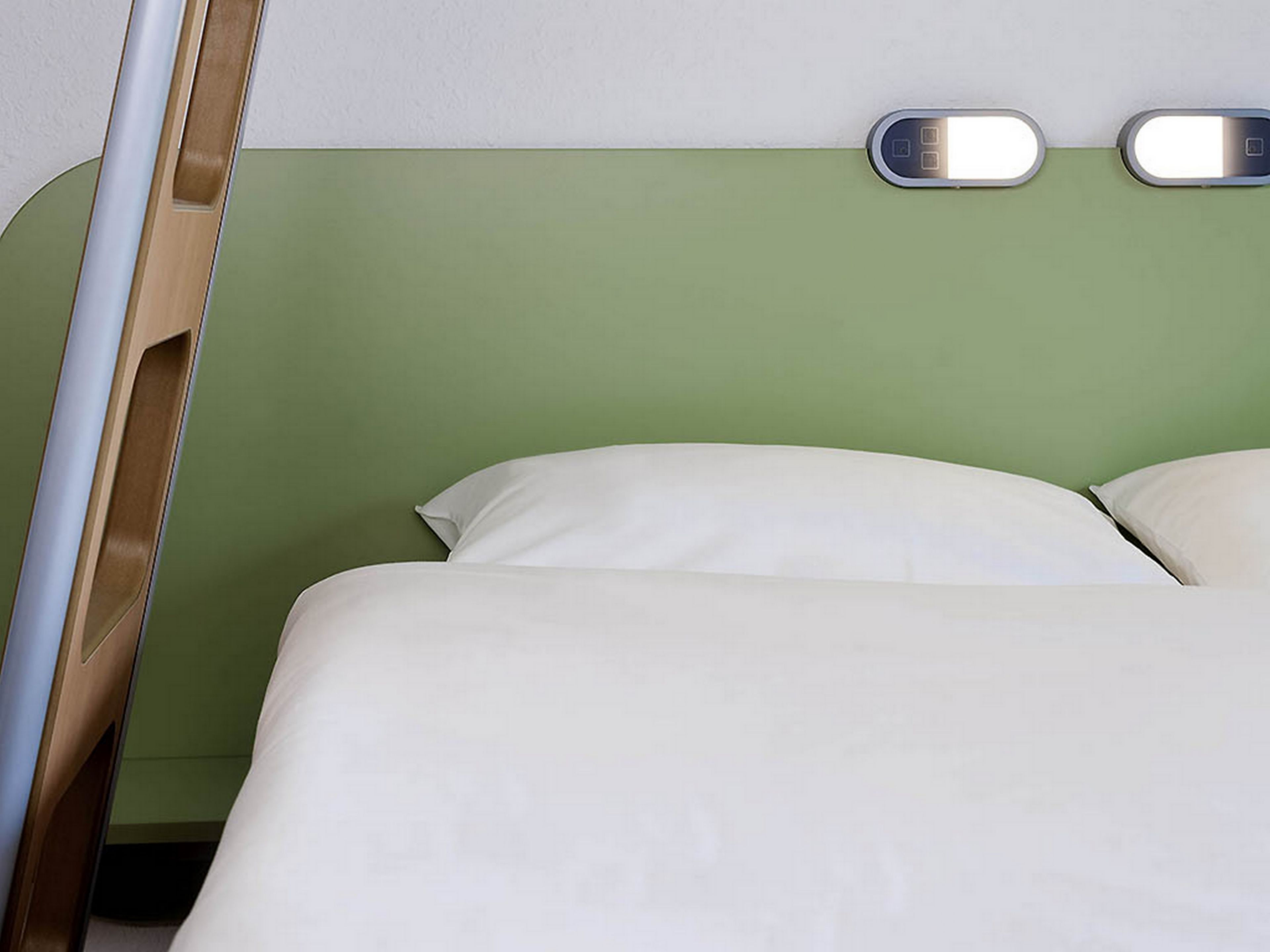 A bed with white bedding and a green wall.
