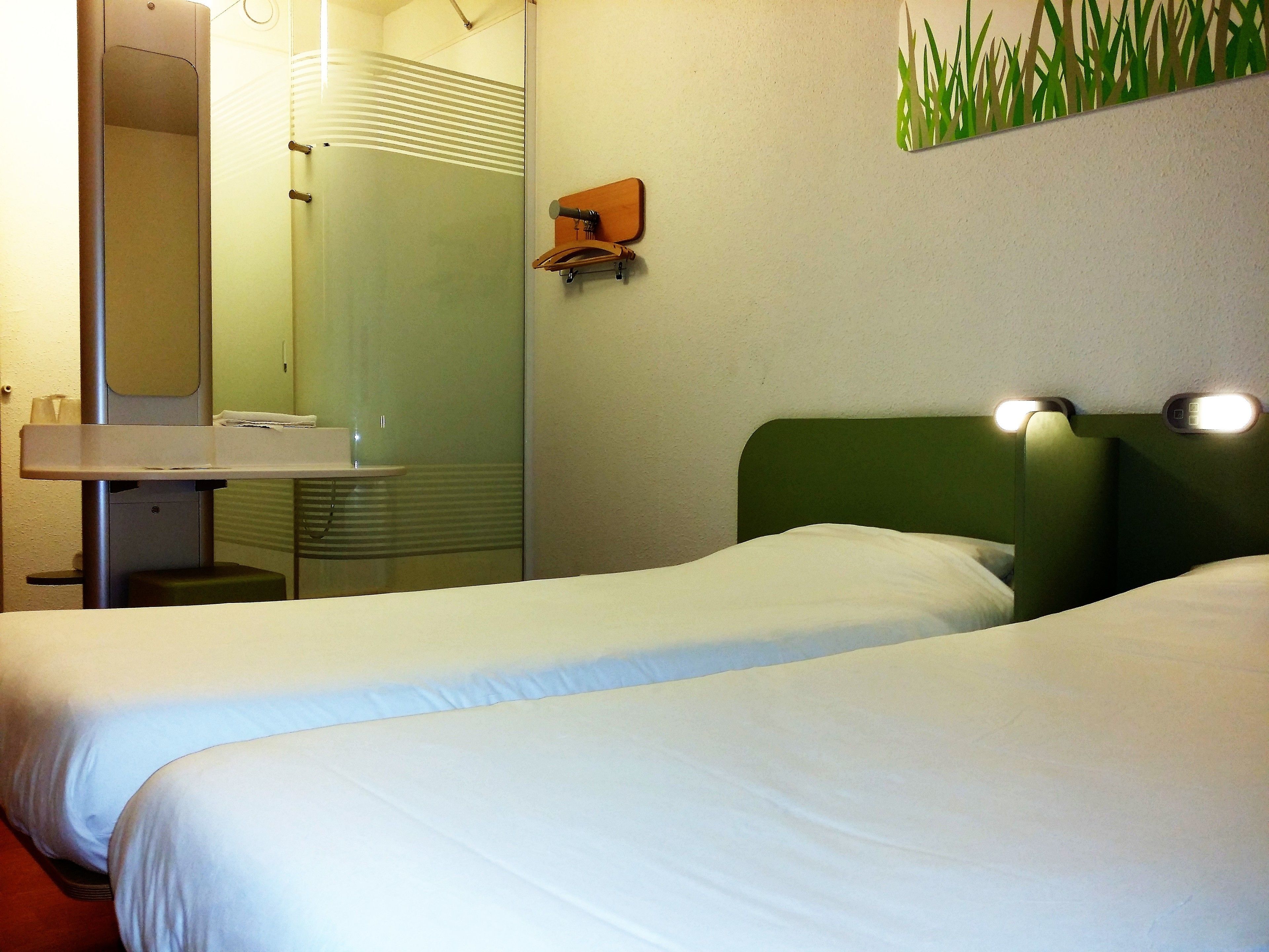 Een hotelkamer met twee eenpersoonsbedden, een klein nachtkastje, een spiegel en een wandplank.