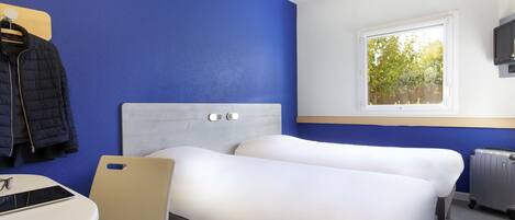 Une chambre d’hôtel avec deux lits, un bureau, une chaise, un porte-manteau et une fenêtre donnant sur des arbres.