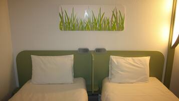 Ett hotellrum med två separata sängar, en grön sänggavel och ett väggmonterat konstverk som föreställer gräs.
