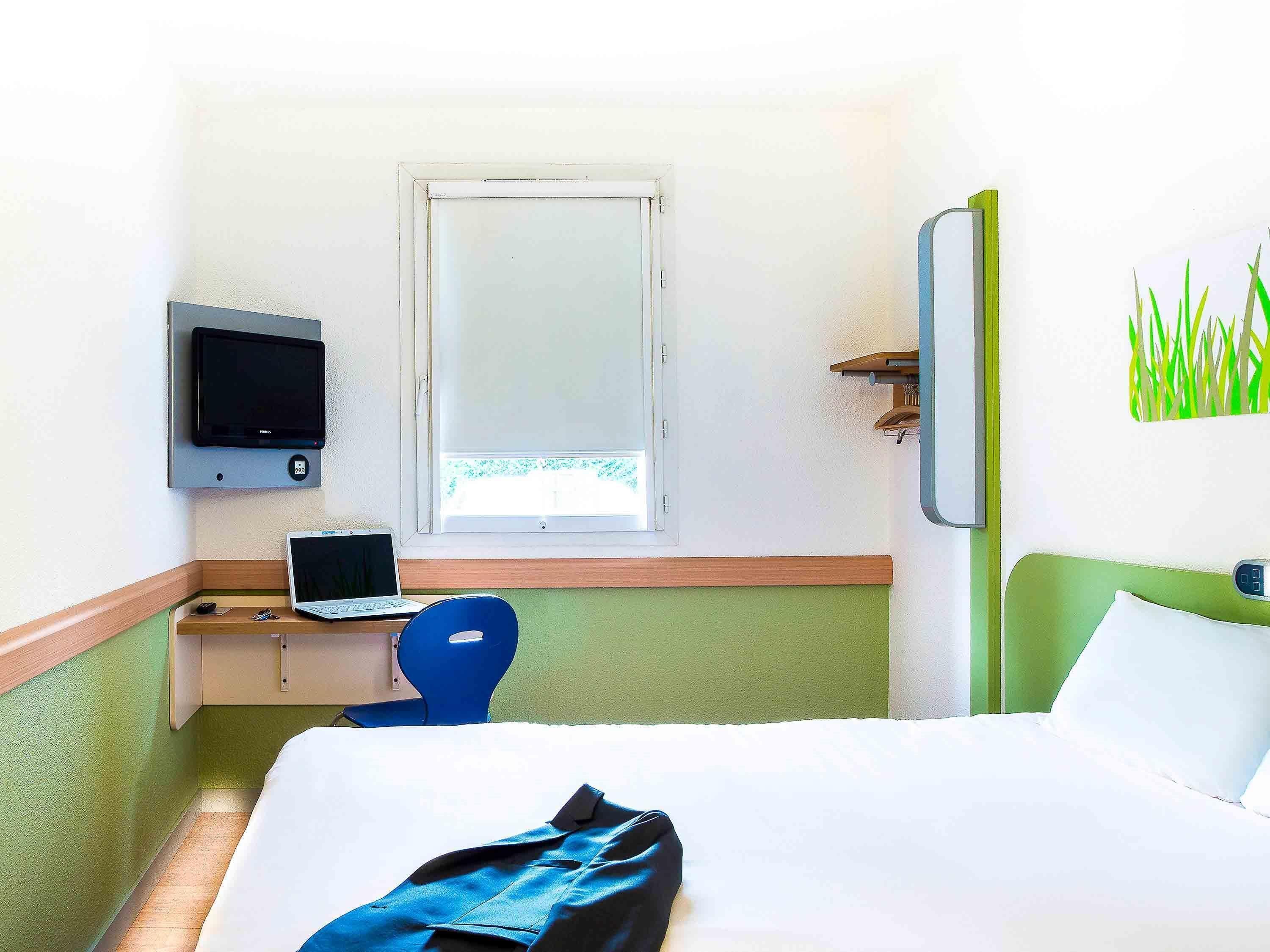 A hotel room with a bed, a desk with a laptop, a television, and a window.