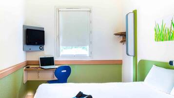 A hotel room with a bed, a desk with a laptop, a television, and a window.