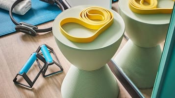 A bathroom with a green stool, a yellow resistance band, a blue towel, and a pair of headphones.