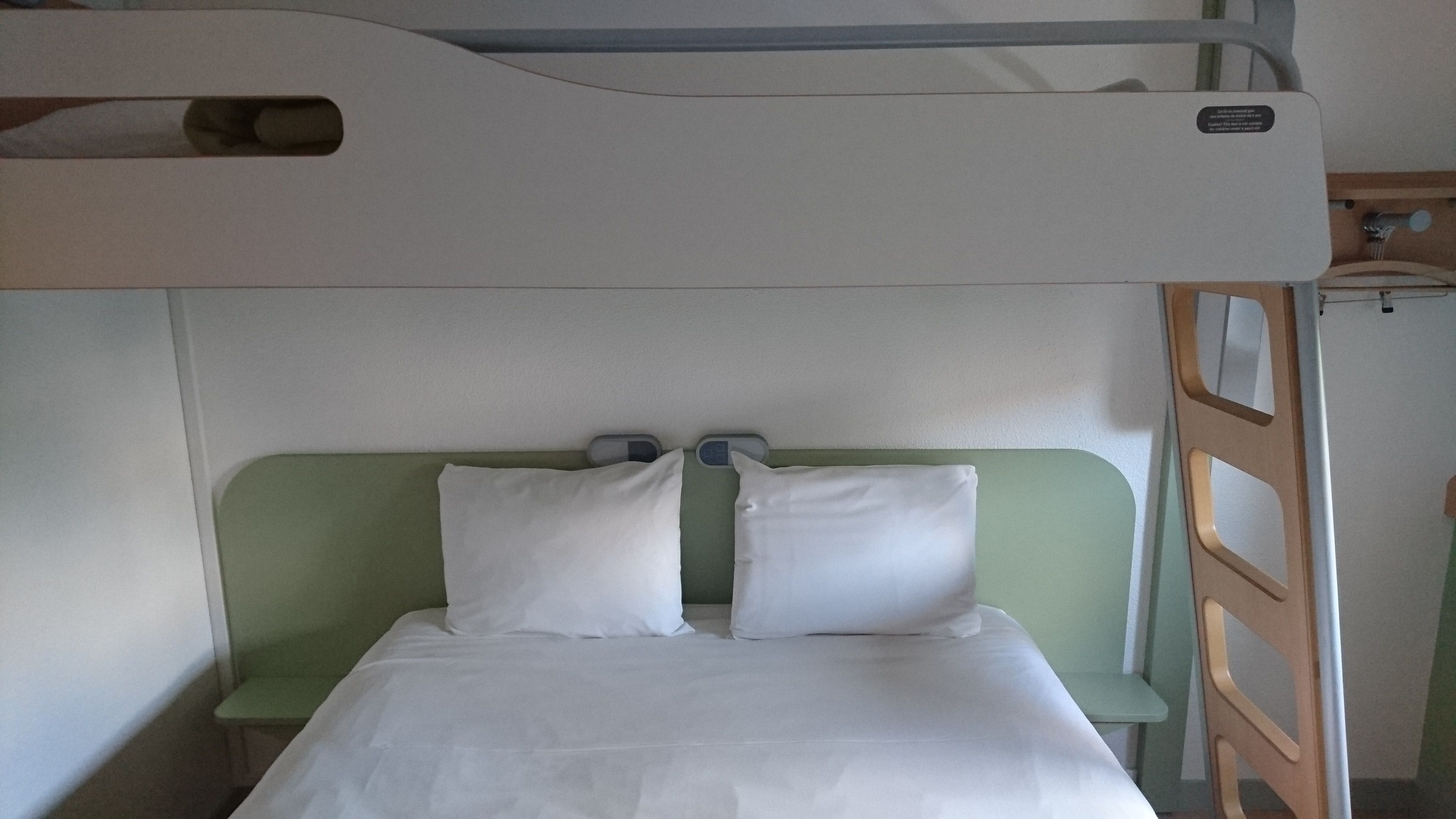 A bunk bed with two pillows, a green headboard, and a small shelf.