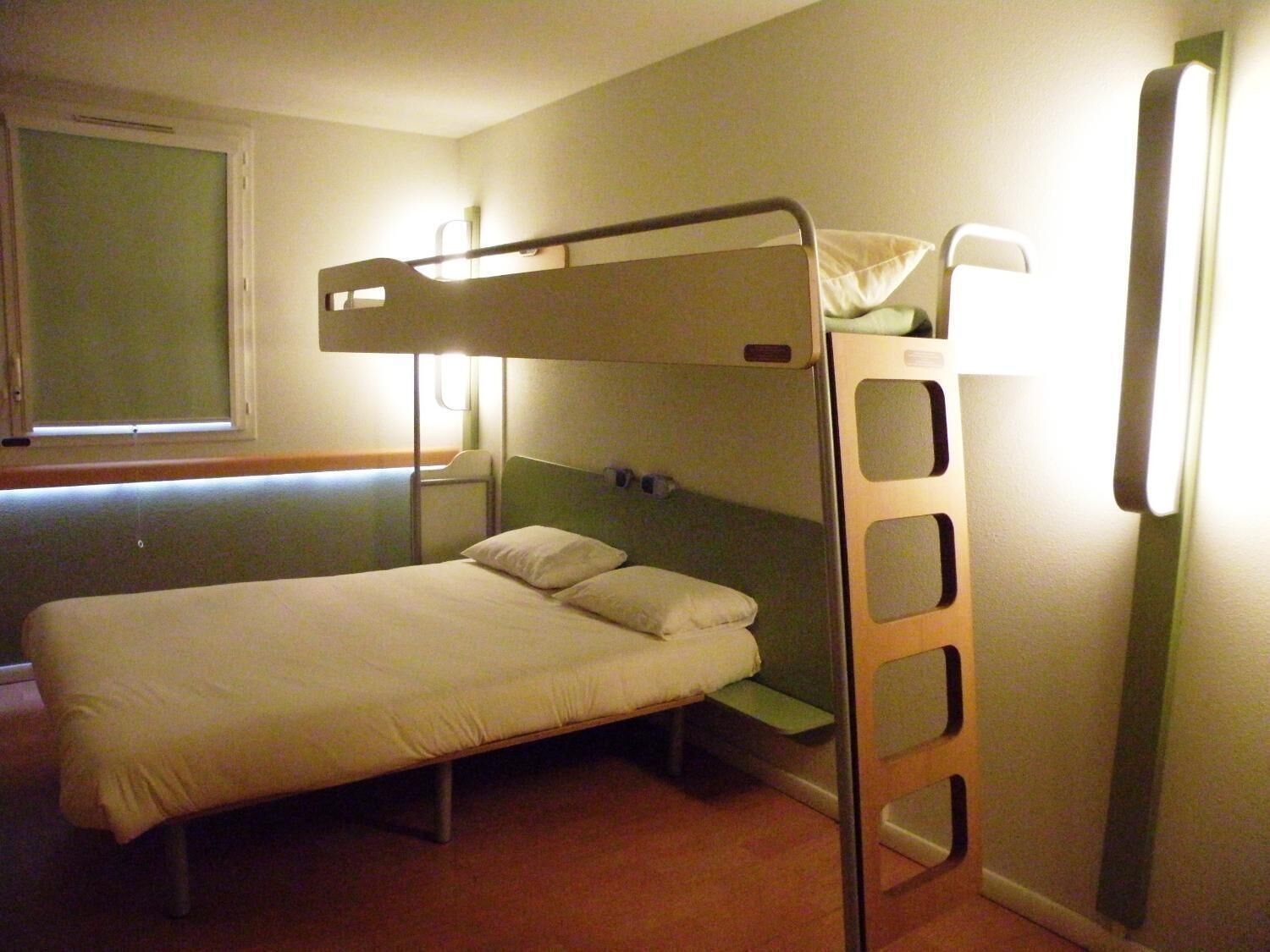 A bunk bed room with a window, a bedside table, and a lamp.