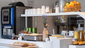 A breakfast bar with coffee machines, a fruit basket, and various food items. - ibis budget Montauban Les Chaumes (Montauban)
