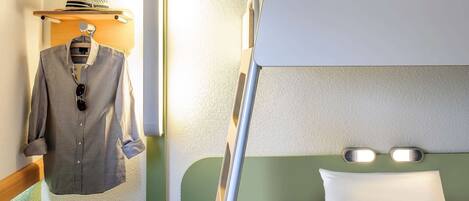 A bunk bed with a green headboard and white bedding, a hanging garment with sunglasses, and a hat on a shelf.
