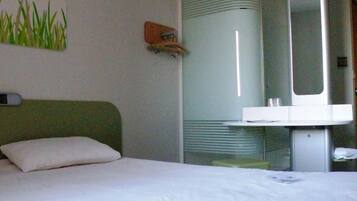 A hotel room with a bed, a small bedside table, a mirror, and a wall-mounted shelf.