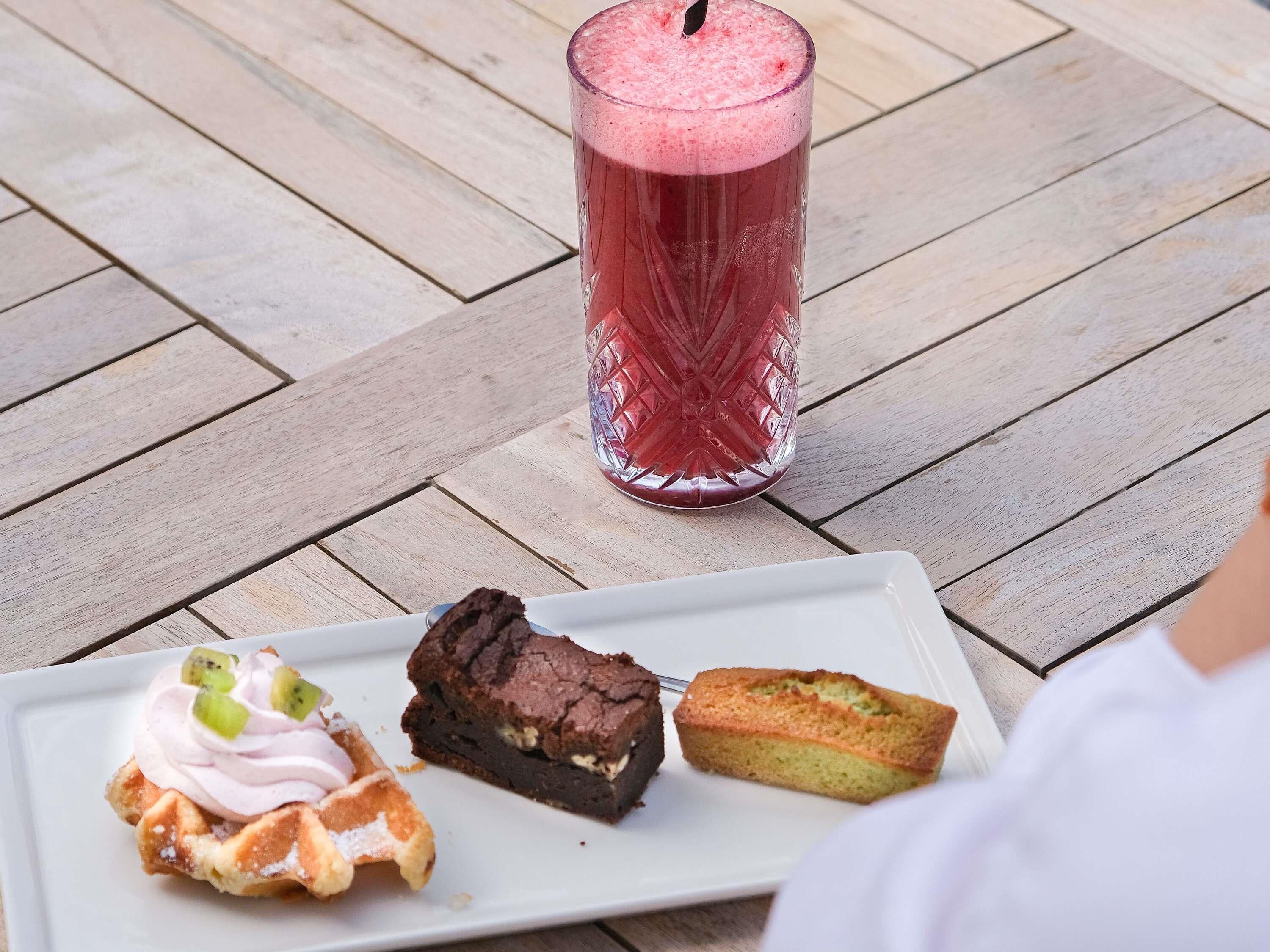 A dessert plate with a waffle, a brownie, and a slice of cake on a wooden table.