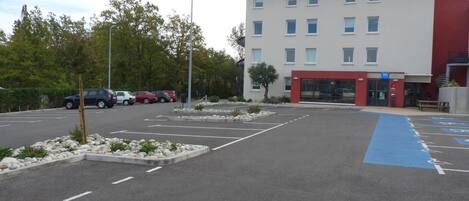 A hotel with an "ibis budget" sign, a parking lot with marked spaces, and a blue handicapped parking space.