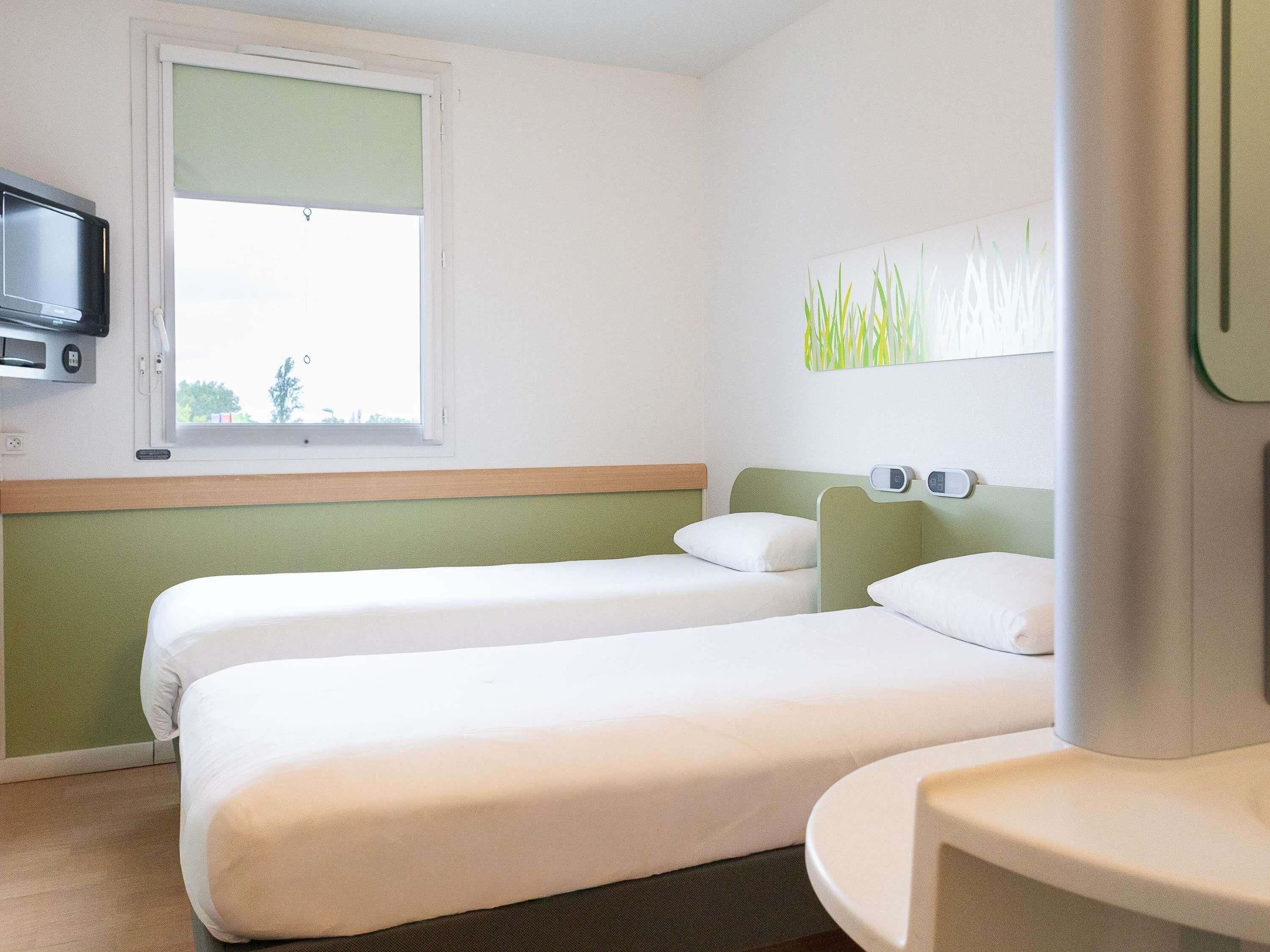 Habitación de hotel con dos camas, ventana, televisor y baño.