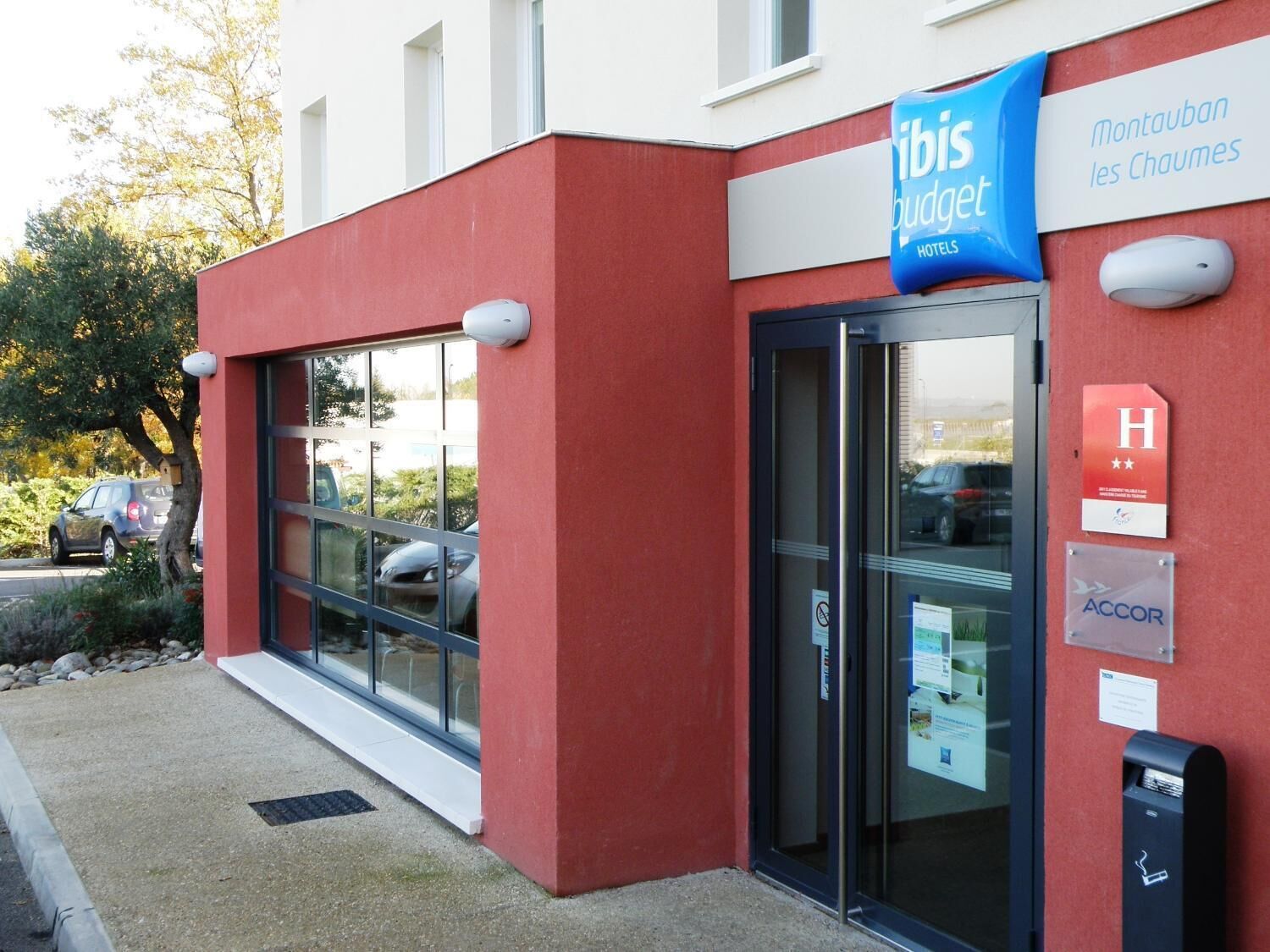 A modern building with a red facade, a glass entrance, and a sign for ibis budget hotels.