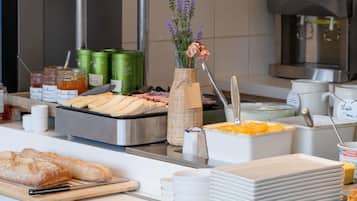 Buffet com diversos alimentos, um vaso de flores e uma pilha de pratos.