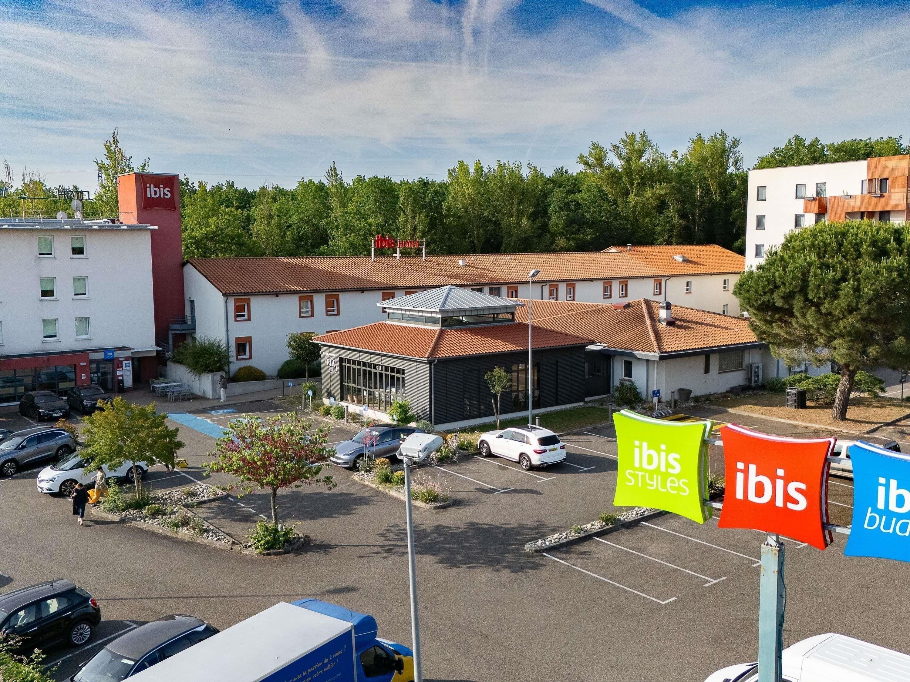 A hotel with a parking lot, a building with a red roof, and a sign for 'ibis Styles'.