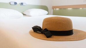A bed with white bedding, a straw hat with a black ribbon, and a green headboard. - ibis budget Montauban Les Chaumes (Montauban)