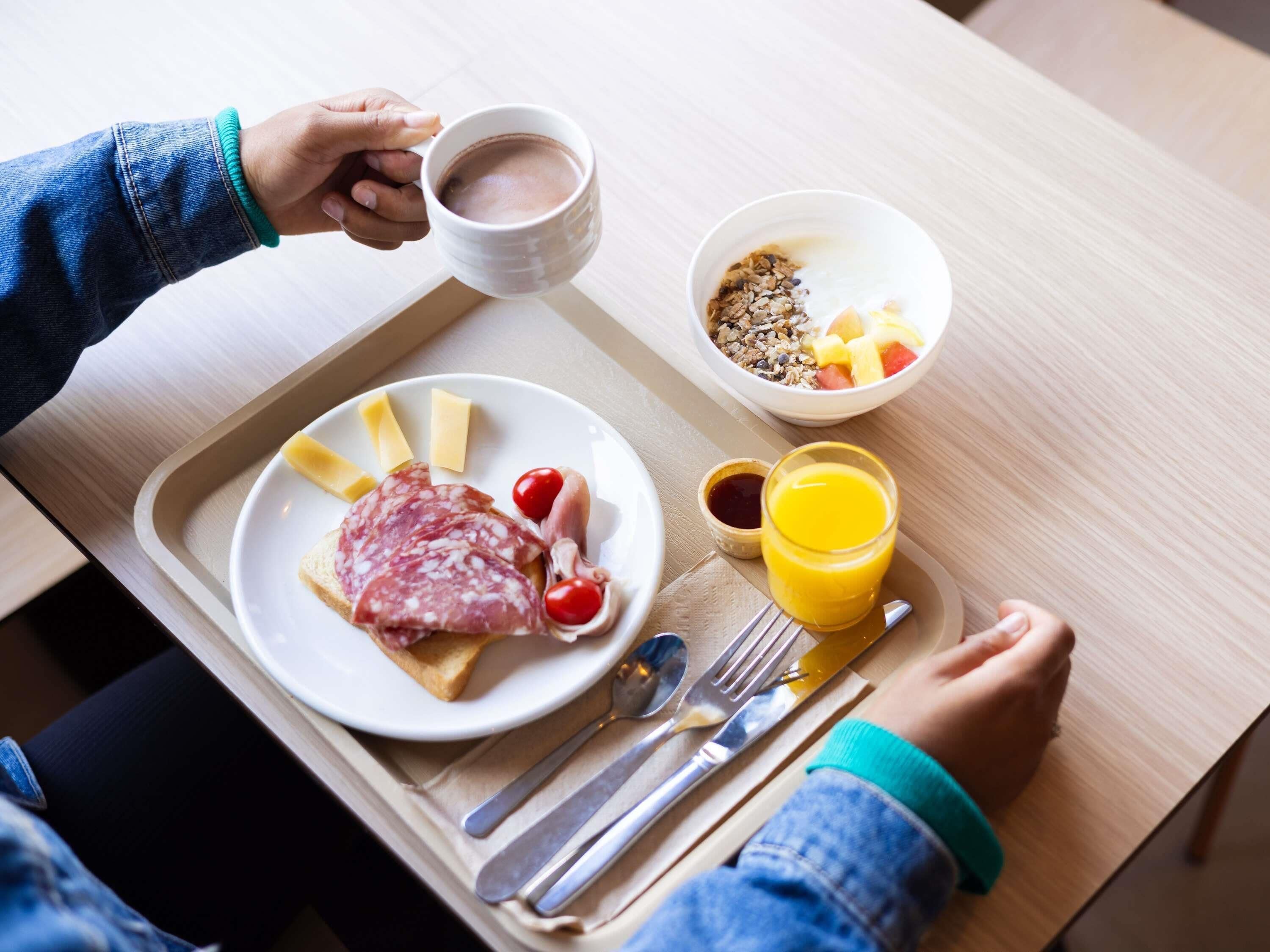 A breakfast tray with a plate of food, a cup of coffee, a bowl of cereal, and a glass of orange juice.
