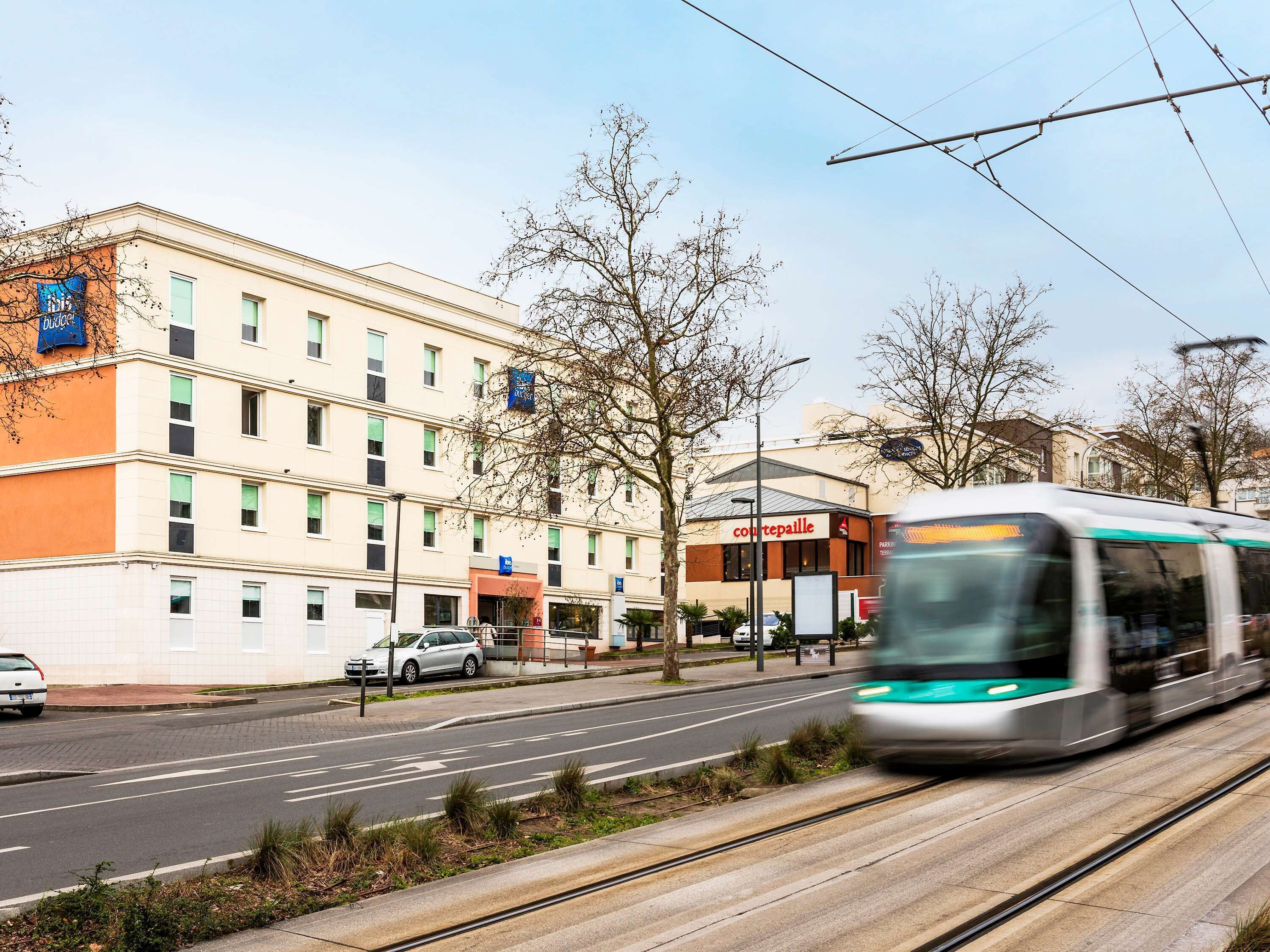 A modern building with multiple floors, a restaurant named "Courtepaille" on the ground floor, and a tram passing by.