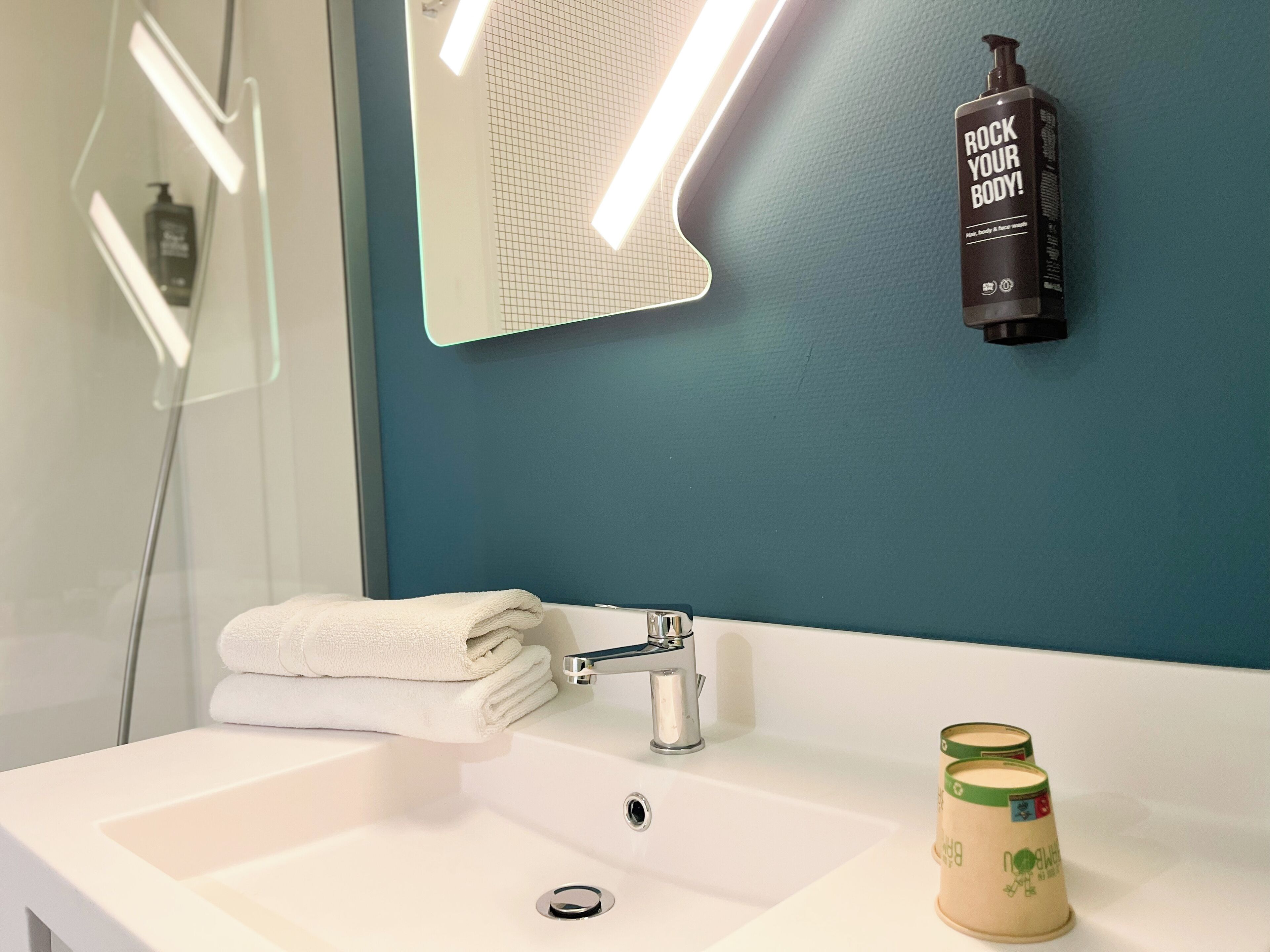 Un baño con un lavamanos blanco, un espejo con diseño de cuadrícula, una botella de jabón corporal y un tarro de loción.