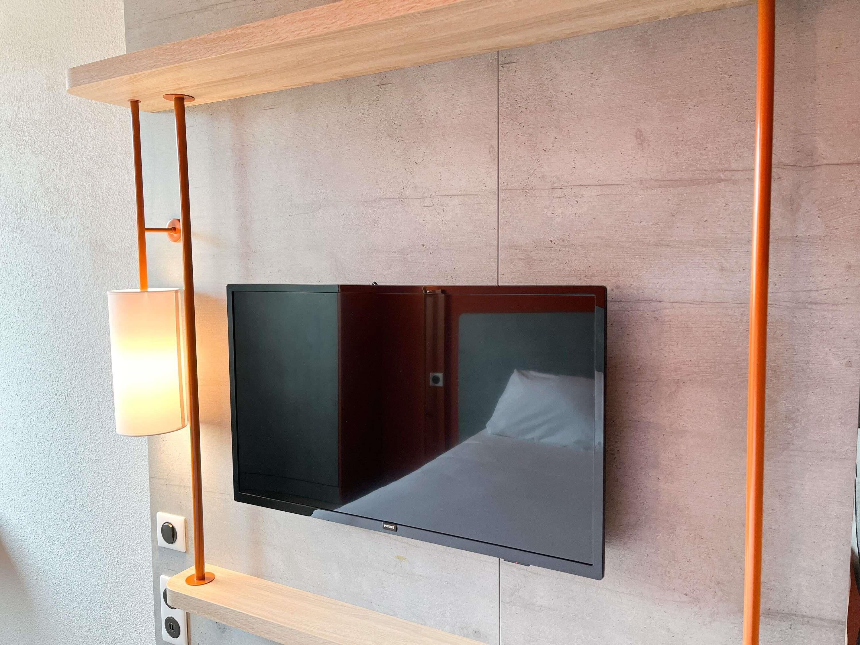 Un téléviseur à écran plat fixé au mur, avec une étagère en bois placée au-dessus.