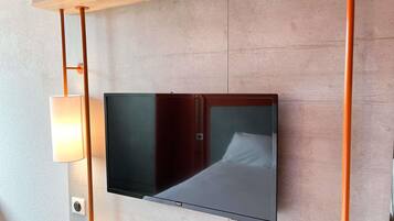 Un téléviseur à écran plat fixé au mur, avec une étagère en bois placée au-dessus.