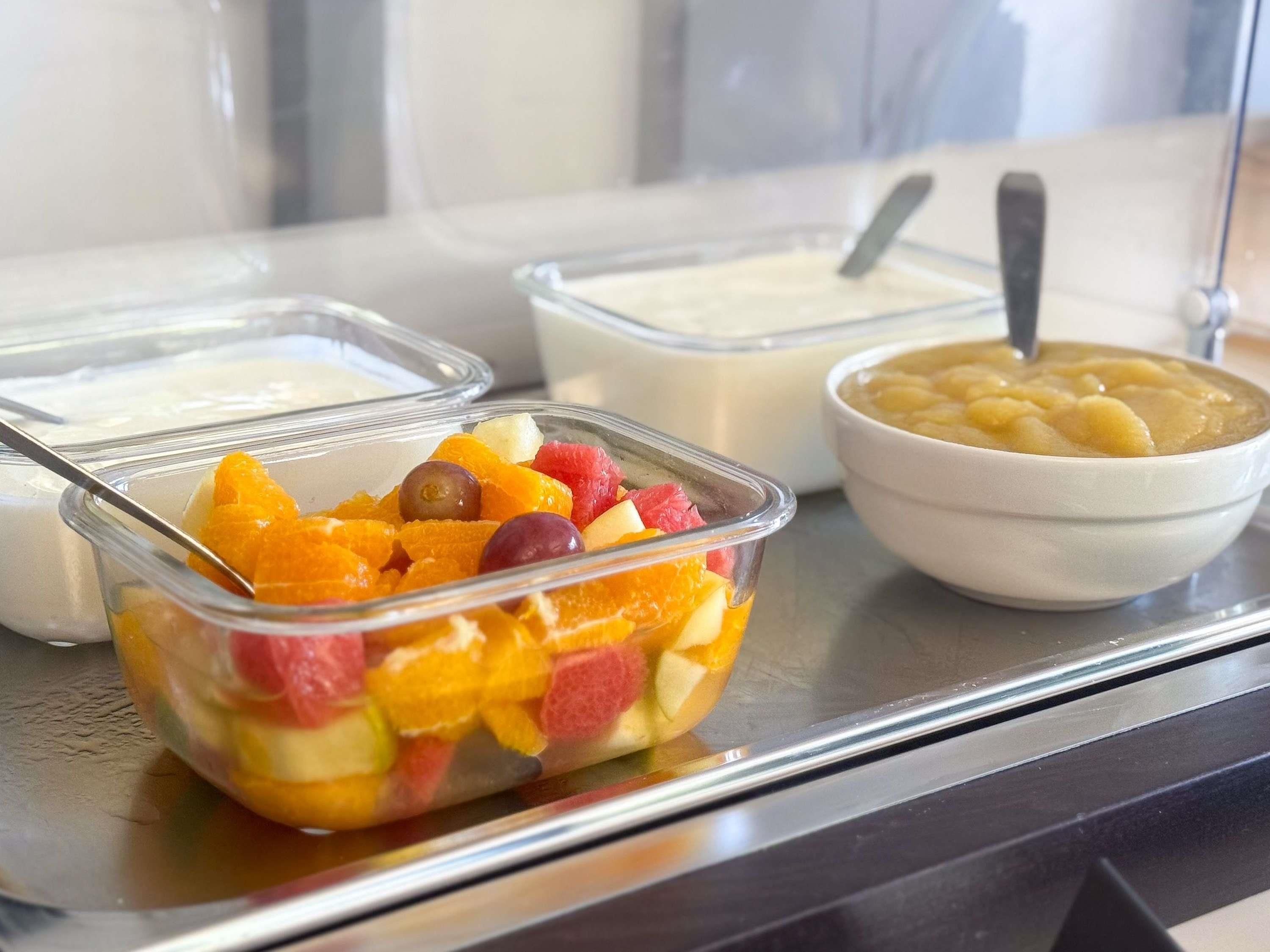 A buffet with various food items including a fruit salad, yogurt, and a bowl of soup.