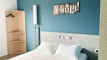 A bedroom with a bed, a wooden wardrobe, a wall-mounted light, and a 'YOUPI!' sign.