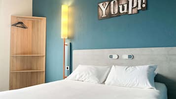 A bedroom with a bed, a wooden wardrobe, a wall-mounted light, and a 'YOUpi!' sign.