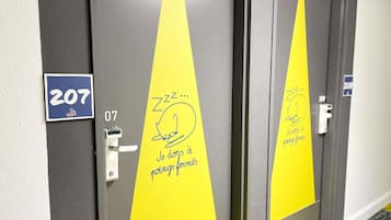 A hotel room door with a number sign, a doorbell, and a yellow sticky note with a cat drawing.