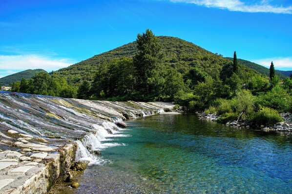 Un río transparente con un lecho pedregoso y una colina al fondo.