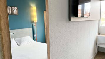 Hotellihuone, jossa on sänky, seinälle asennettu televisio ja seinävalaisin.