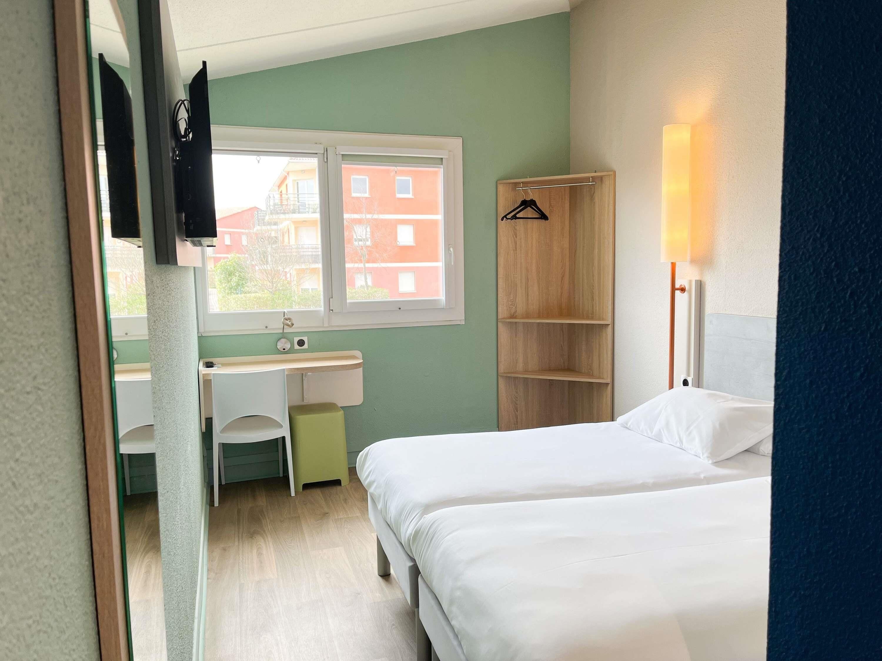 A bedroom with a bed, a desk, a chair, a hanging light, and a window.