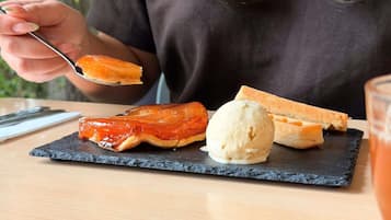 Eine Person hält einen Löffel mit einer Portion Speise, einem runden Dessert und zwei Brotscheiben auf einem Schieferteller.