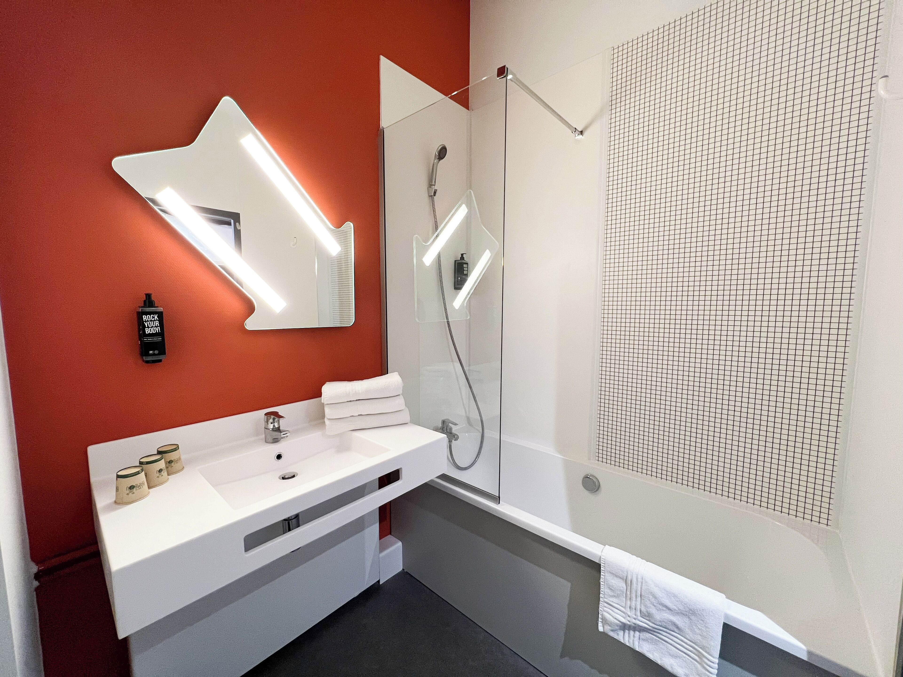 Un baño moderno con un tocador blanco, un espejo grande, una ducha con puerta de cristal y una pared con diseño.