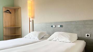 Ein Hotelzimmer mit zwei Betten, einem Holzschrank, einer Nachttischlampe und einer wandmontierten Steuerung.