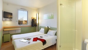 A hotel room with two beds, a television, a window with a view, a shower, and a towel rack. - First Inn Hotel (Apt)