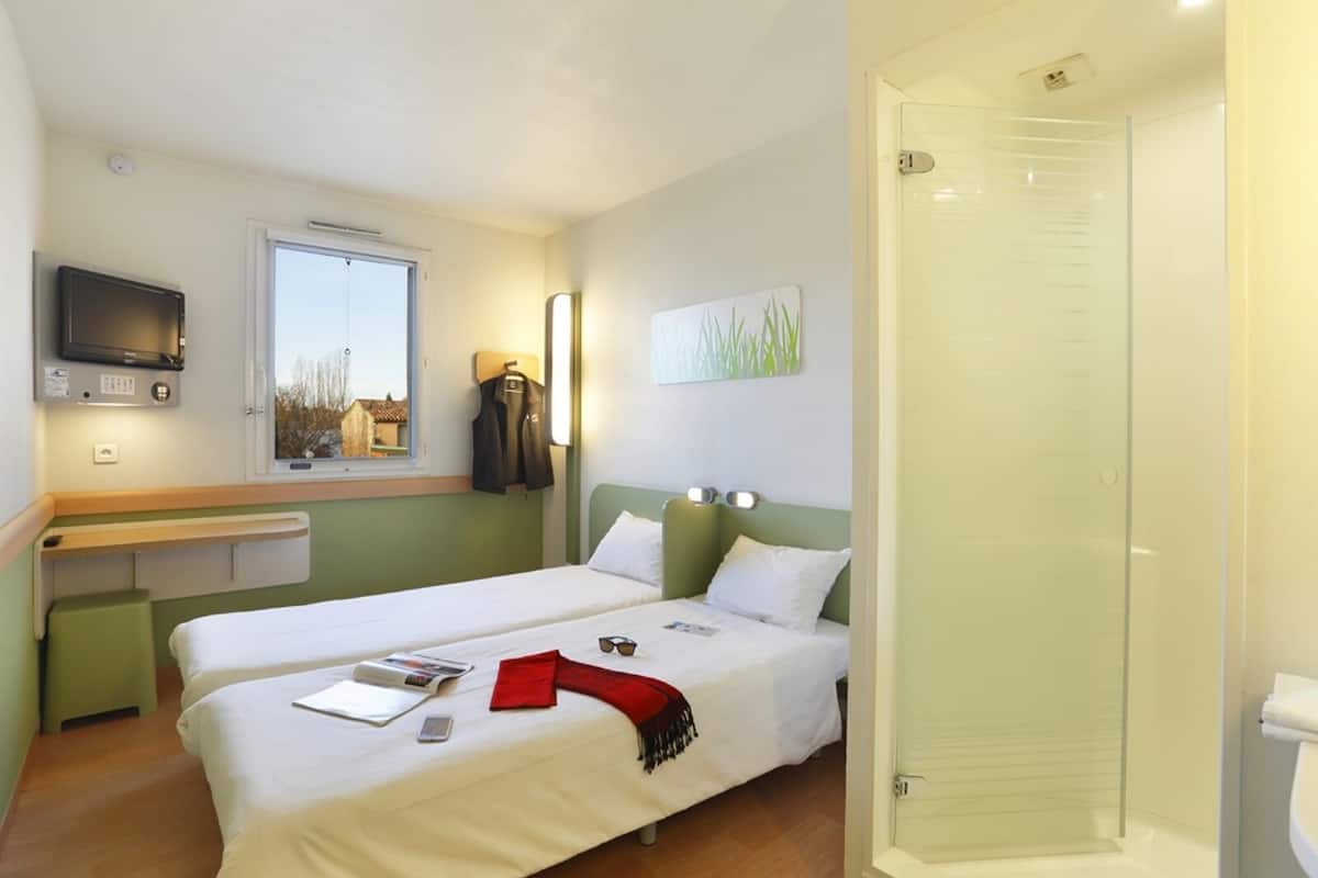 A hotel room with two beds, a television, a window with a view, a shower, and a towel rack.