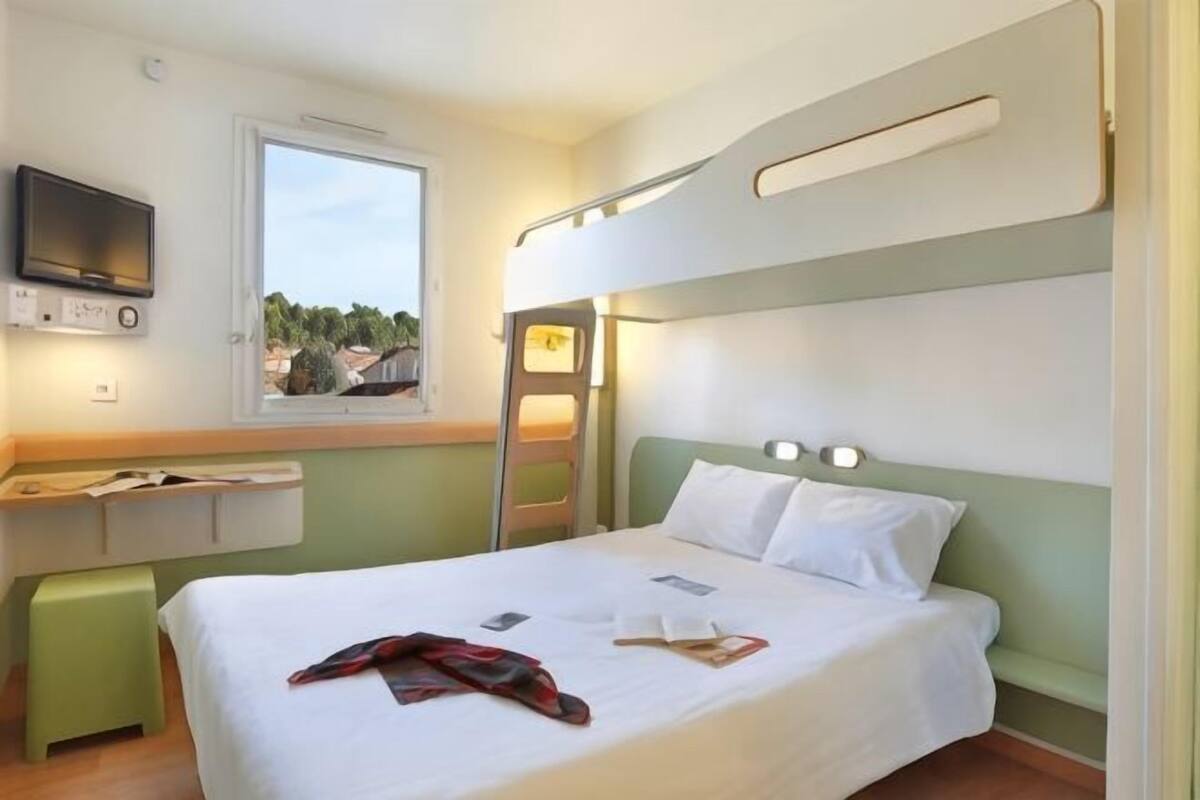 A hotel room with a bed, a desk with a chair, a television, and a window with a view.