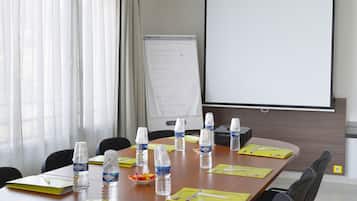 Ein Konferenzraum mit einem großen Tisch, Stühlen, einer Projektionsleinwand, einer Whiteboard und Wasserflaschen.