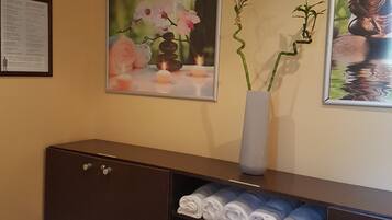 Habitación de hotel con cama, cómoda de madera oscura, un florero con planta y dos cuadros en la pared.