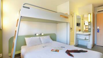 Une chambre d’hôtel avec un lit superposé, une table de chevet avec un livre et un téléphone, une salle de bain avec un lavabo et un miroir, et une porte avec une pancarte.