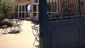 A gated entrance with a building in the background, outdoor seating area, and a sign indicating a business or service. - First Inn Hotel (Apt)