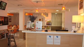 A reception area with a counter, chairs, a plant, and informational posters. - First Inn Hotel (Apt)