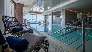 Une piscine intérieure dotée de chaises longues et offrant une vue sur l’extérieur.