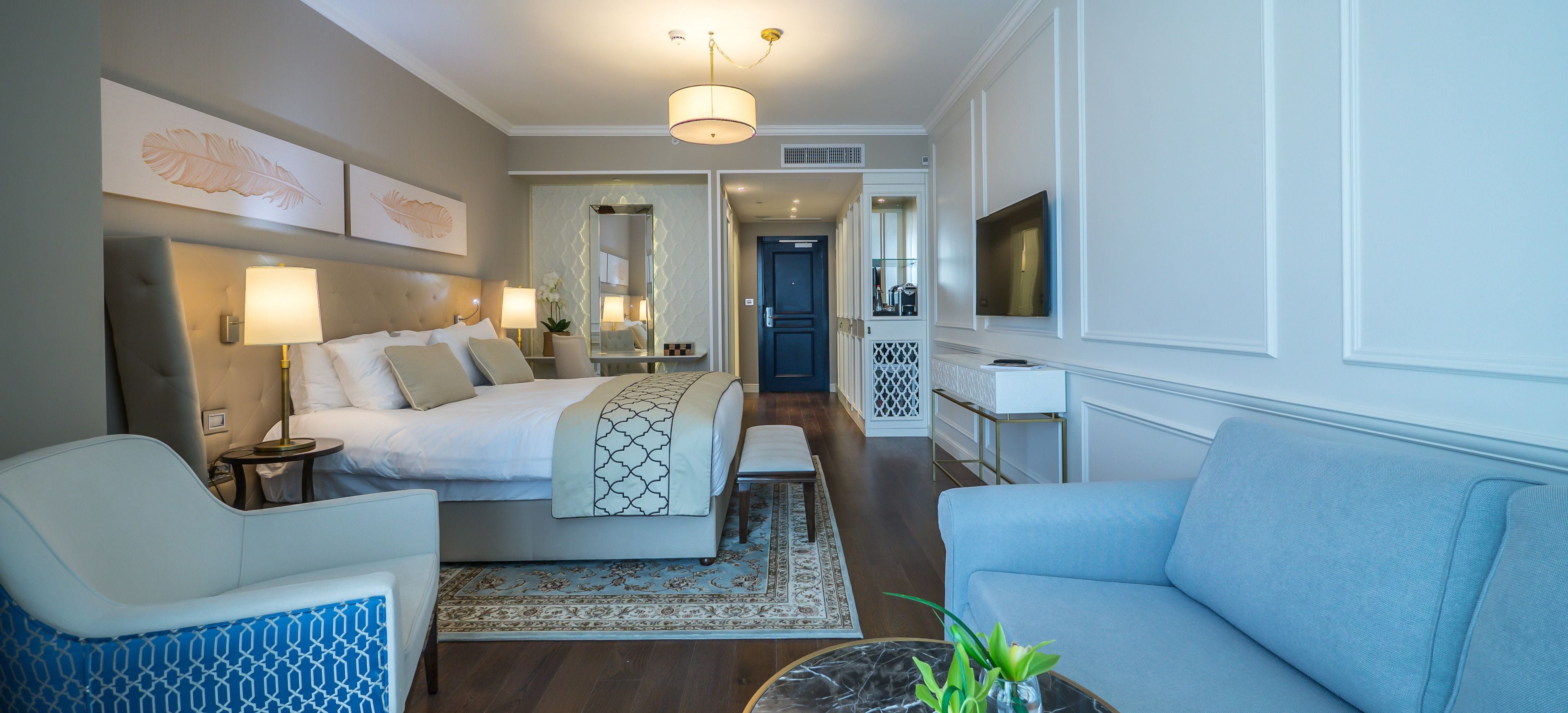 Habitación de hotel con cama, sofá, sillón, televisor y escritorio con espejo.