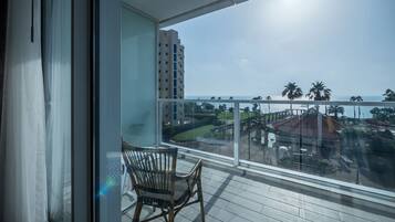 Enjoy the breathtaking view of the coastal area from this balcony, featuring a wicker chair and glass railing.
