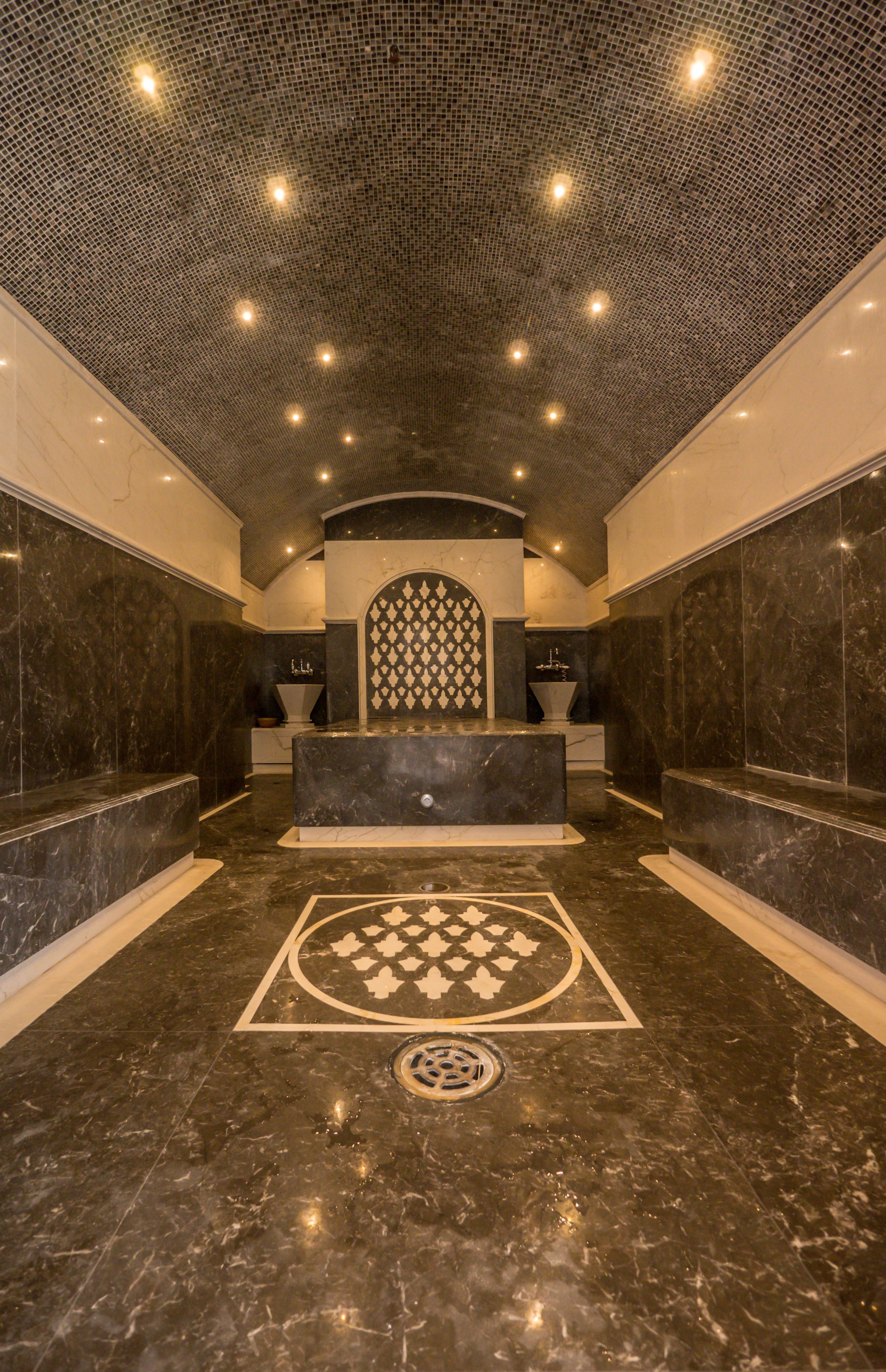 A modern bathroom with a central sink, dark marble flooring, and a patterned ceiling.